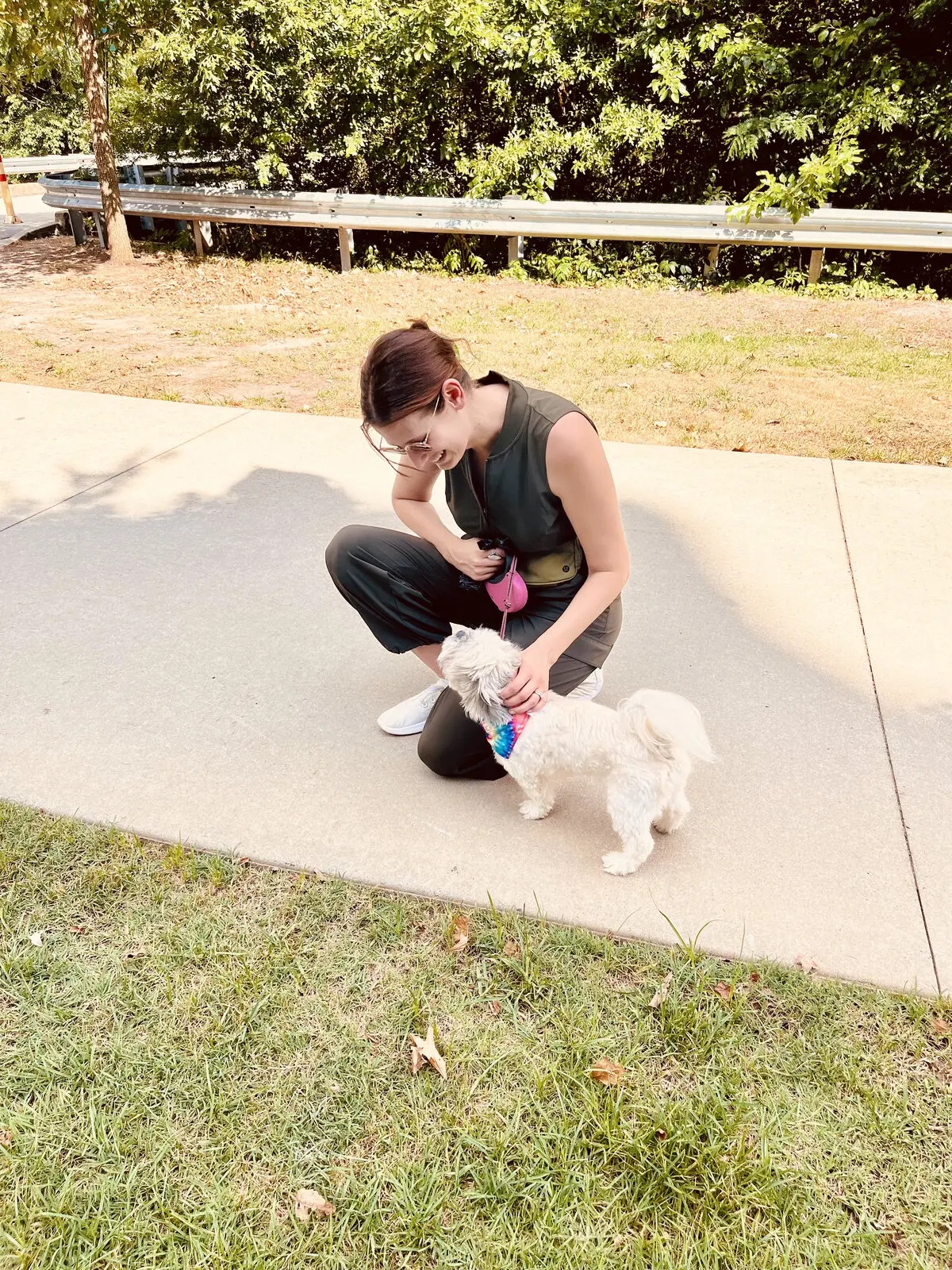 Kimberly crouching on a sidewalk to pet a fluffy white pup