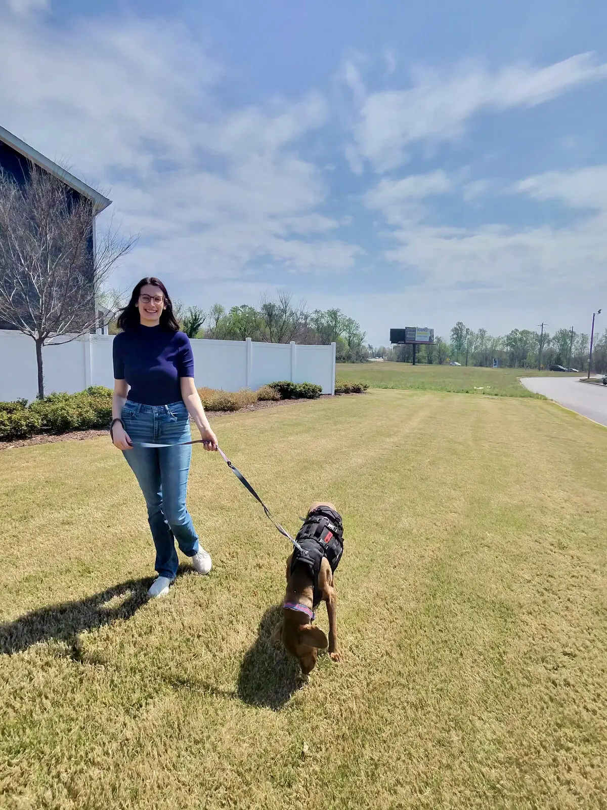 Kimberly walking a small dog on a leash across a sunny lawn